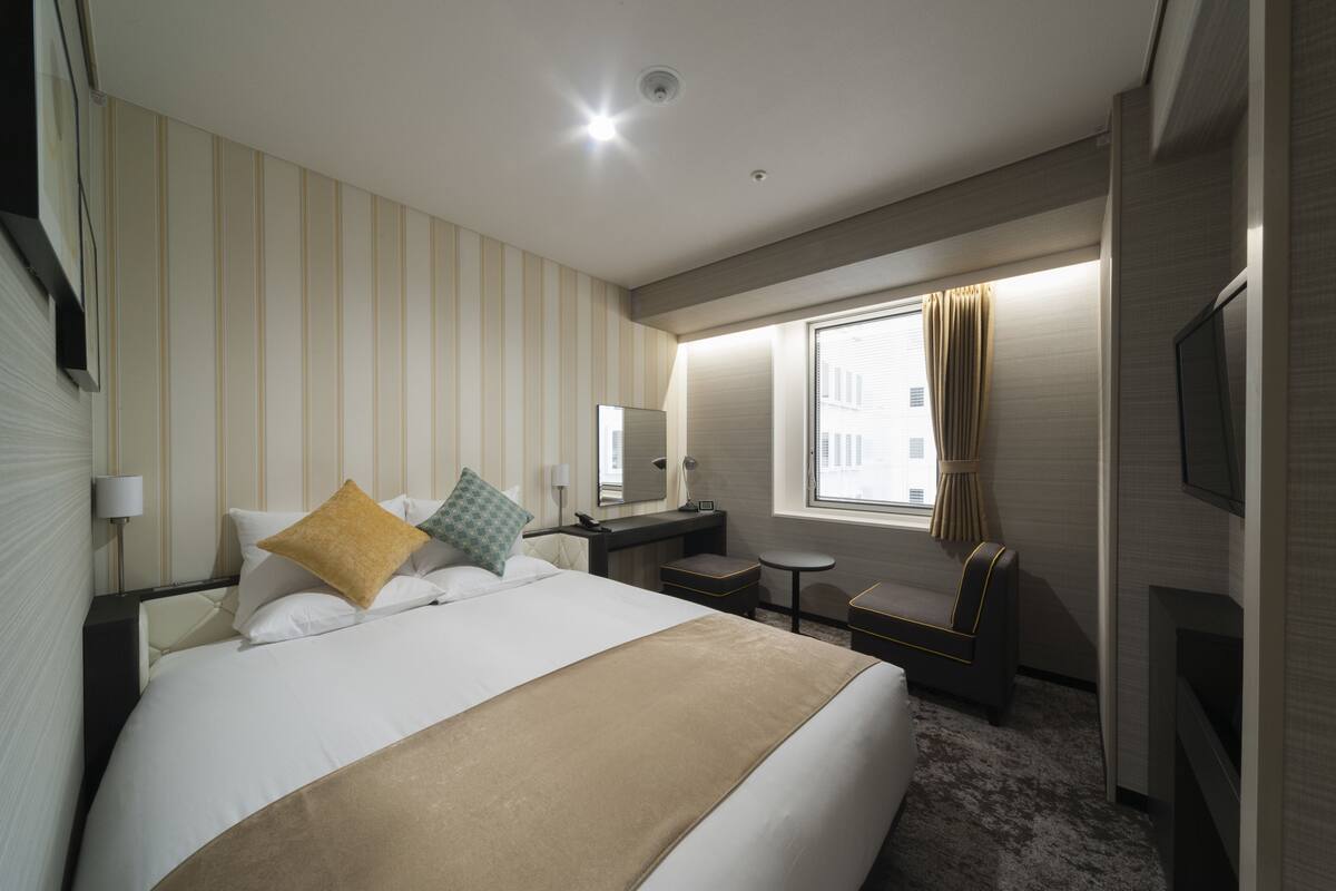 A hotel room with a large bed, a desk, a chair, a TV, and a window with curtains.