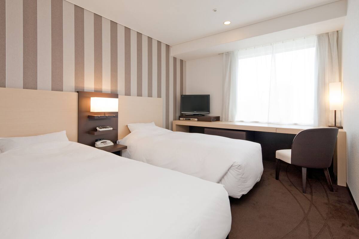 A hotel room with two beds, a desk, a television, and a chair.