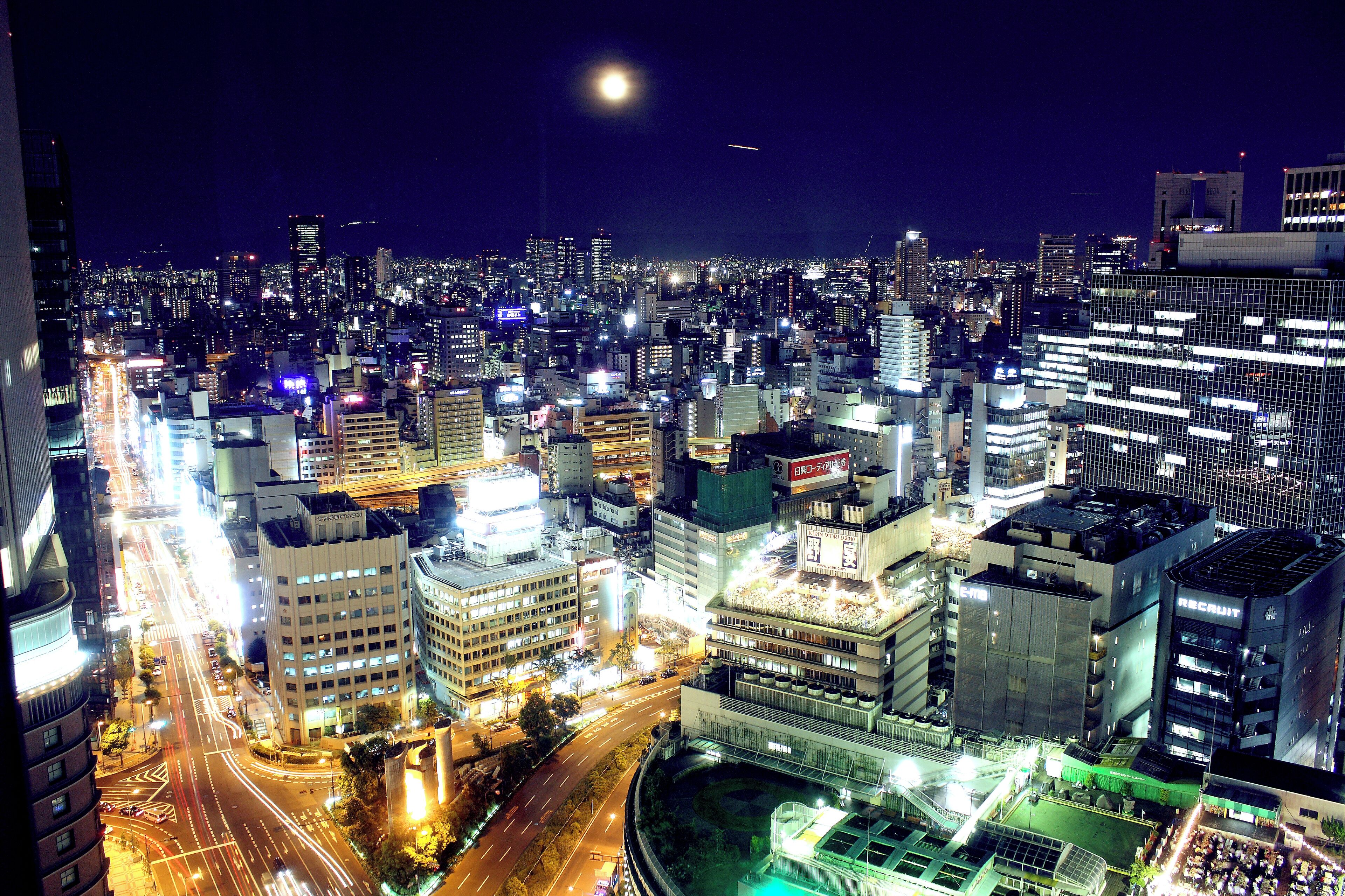 A nighttime cityscape with illuminated buildings and a crescent moon.