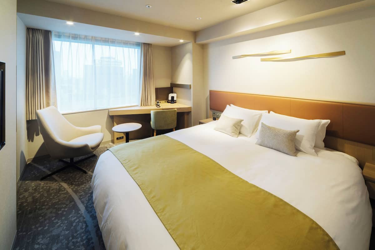 A hotel room with a large bed, a desk, a chair, and a window with curtains.