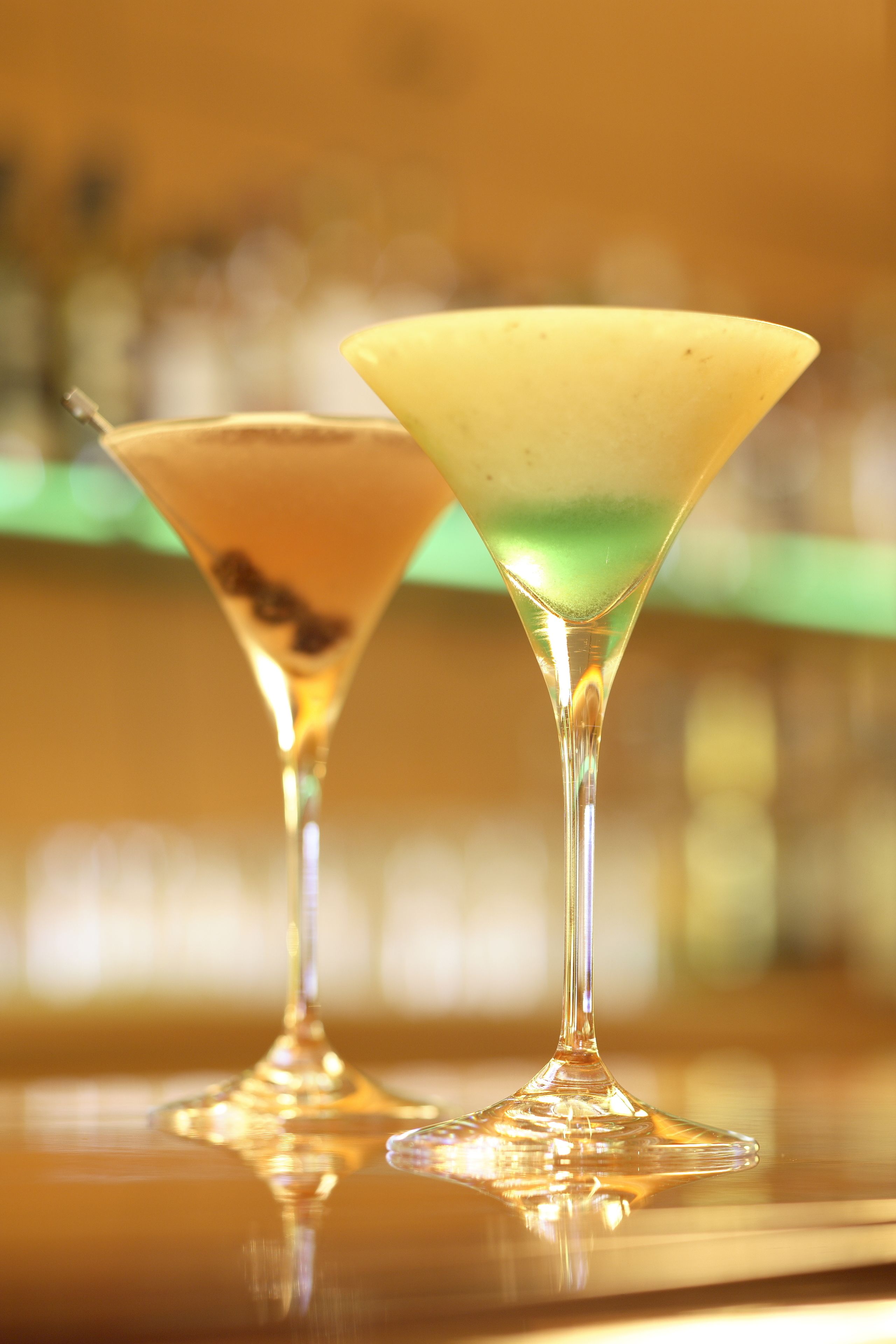 Two martini glasses on a reflective surface with a blurred background.