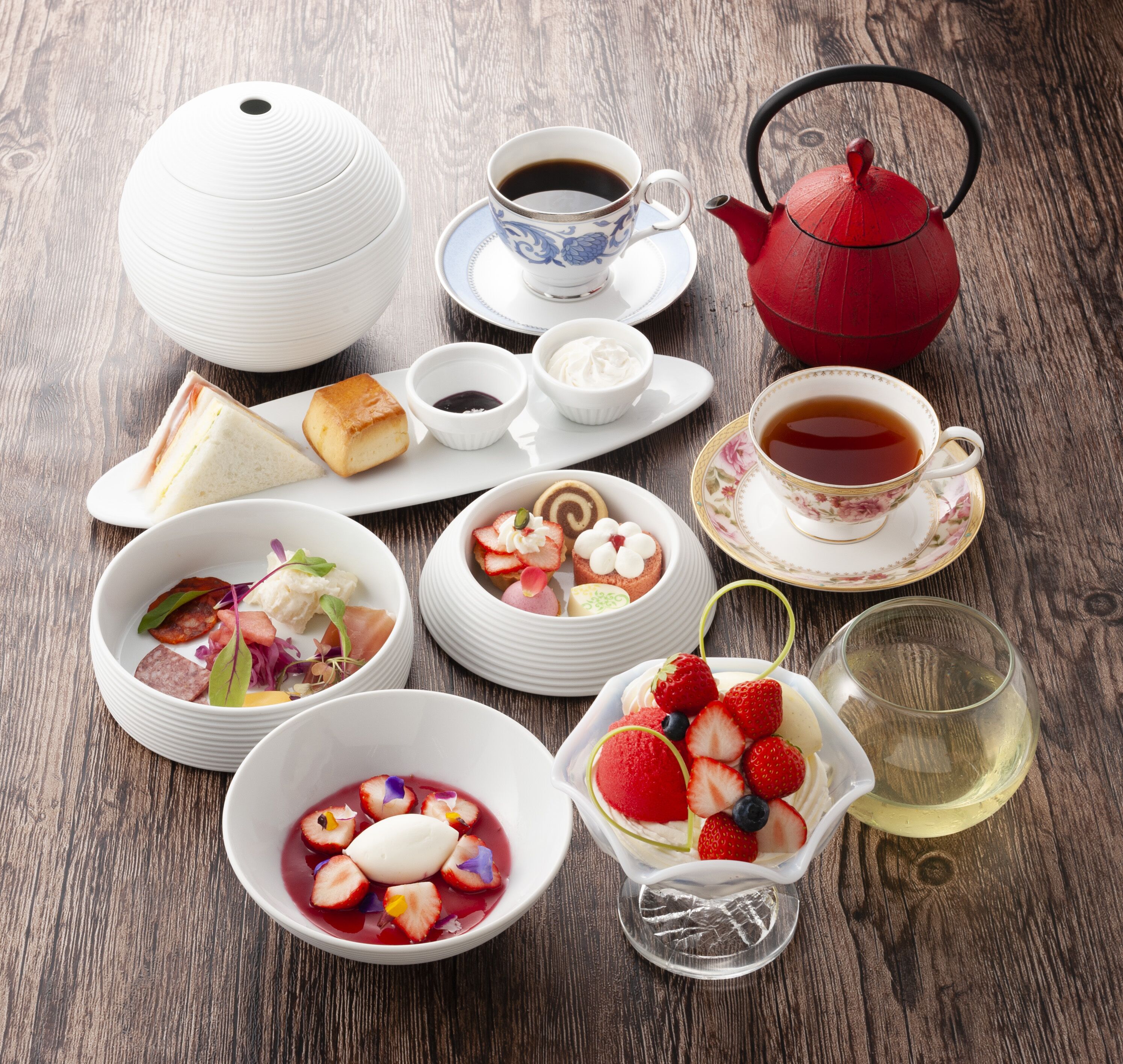 Variedad de alimentos y bebidas sobre una mesa de madera, incluyendo una tetera, tazas y cuencos con postres.