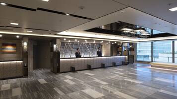 A modern reception area with a marble floor, a reception desk, and a staircase leading to an upper level.