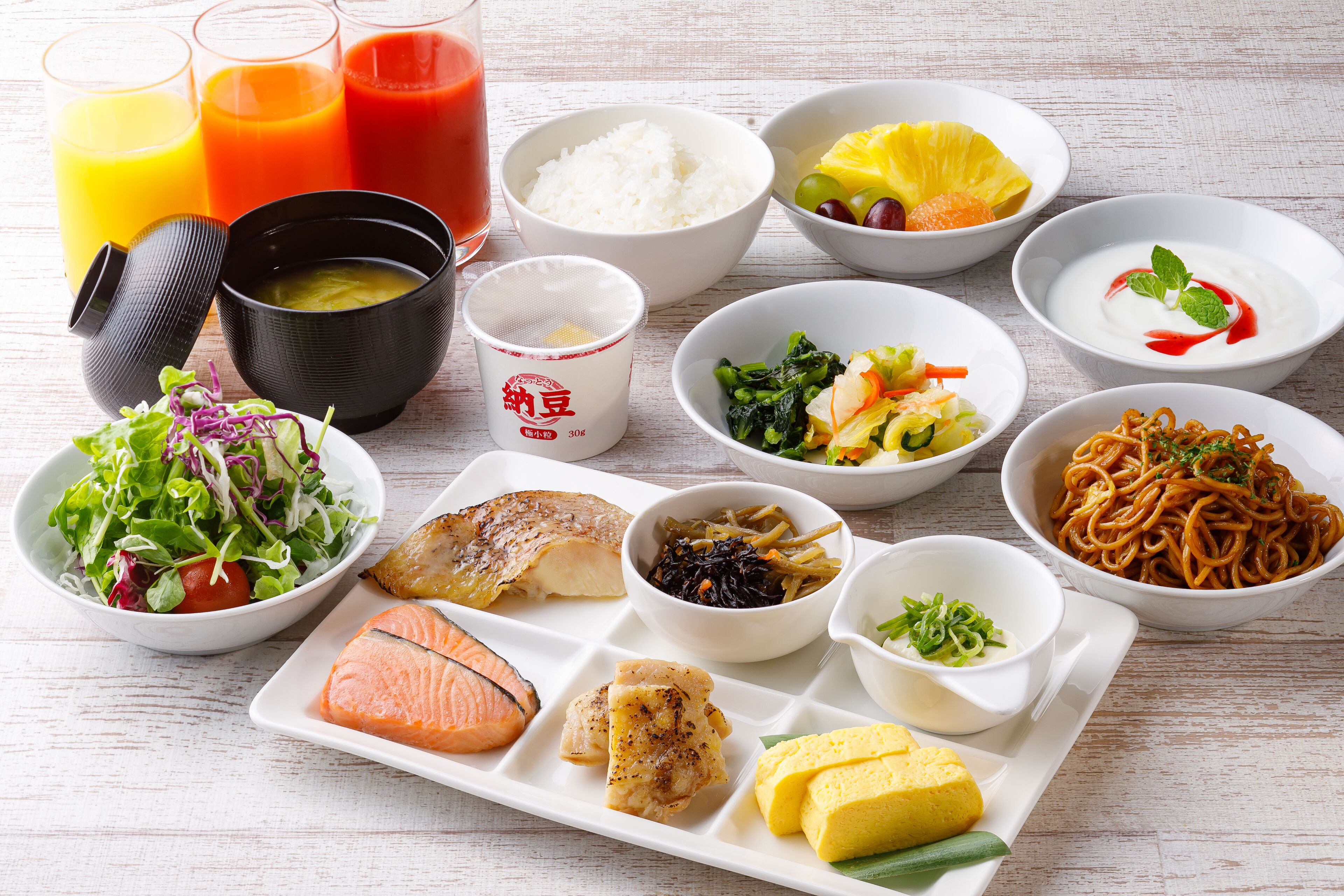 A variety of dishes including sushi, rice, and noodles, arranged on a white tray.