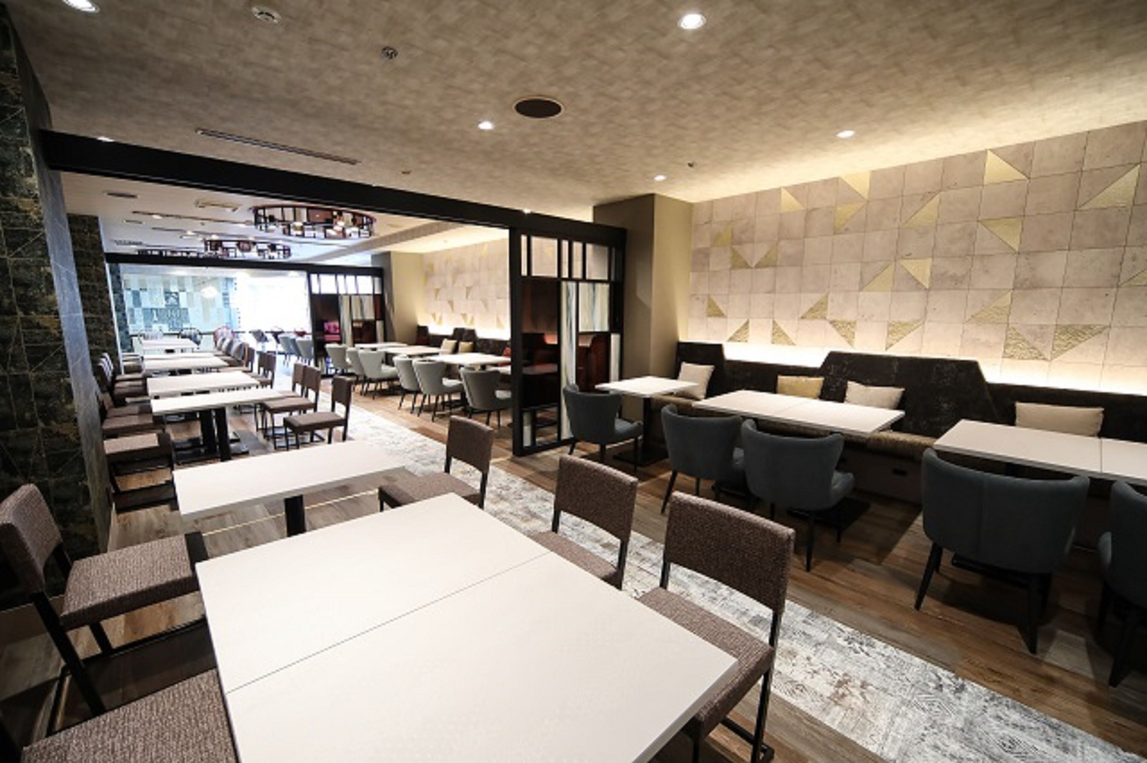A modern restaurant interior with multiple dining tables and chairs, a patterned wall, and a view of the dining area through a glass partition.