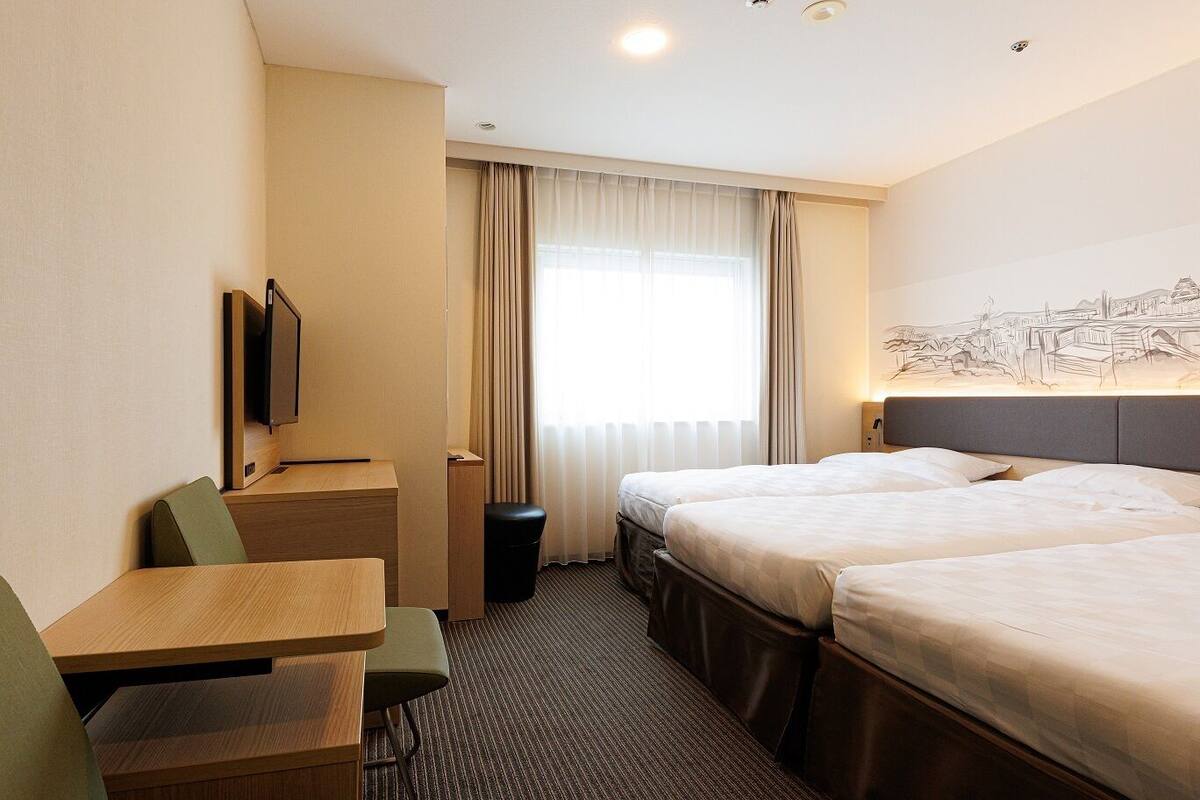 A hotel room with two beds, a desk, a chair, a TV, and a window with curtains.