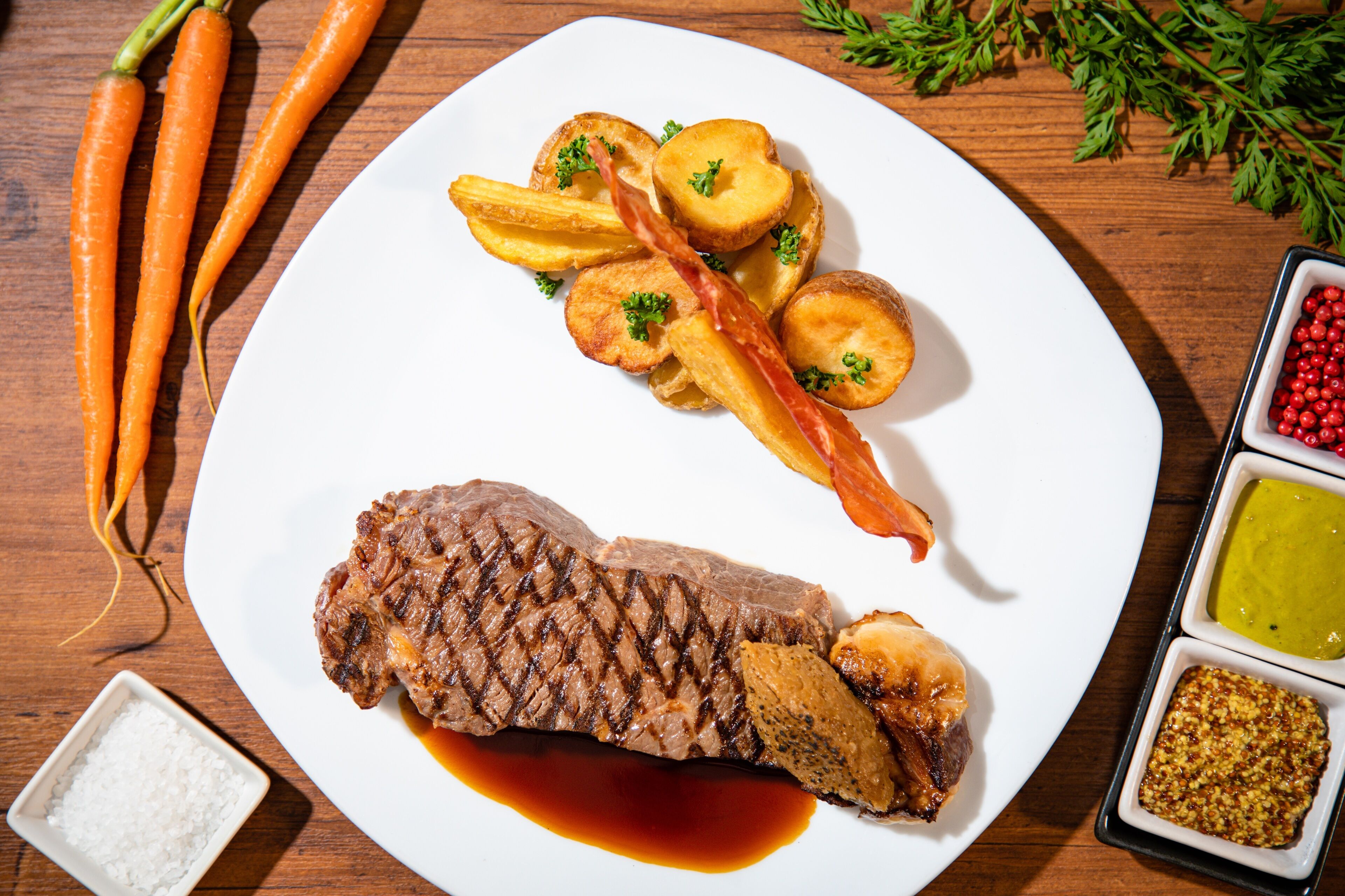 Een bord met steak, geroosterde aardappelen en wortelen.