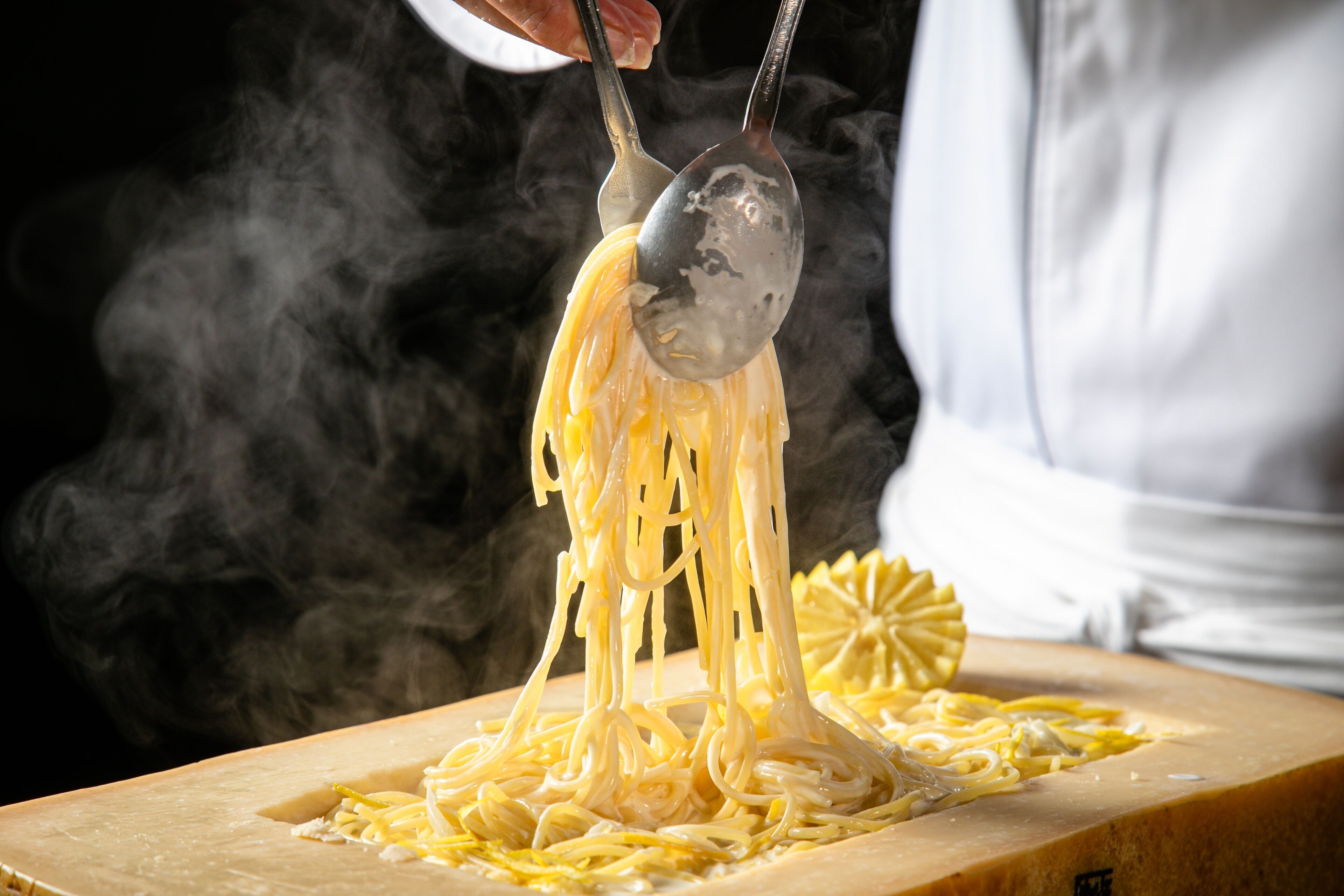 A person grating cheese over pasta.
