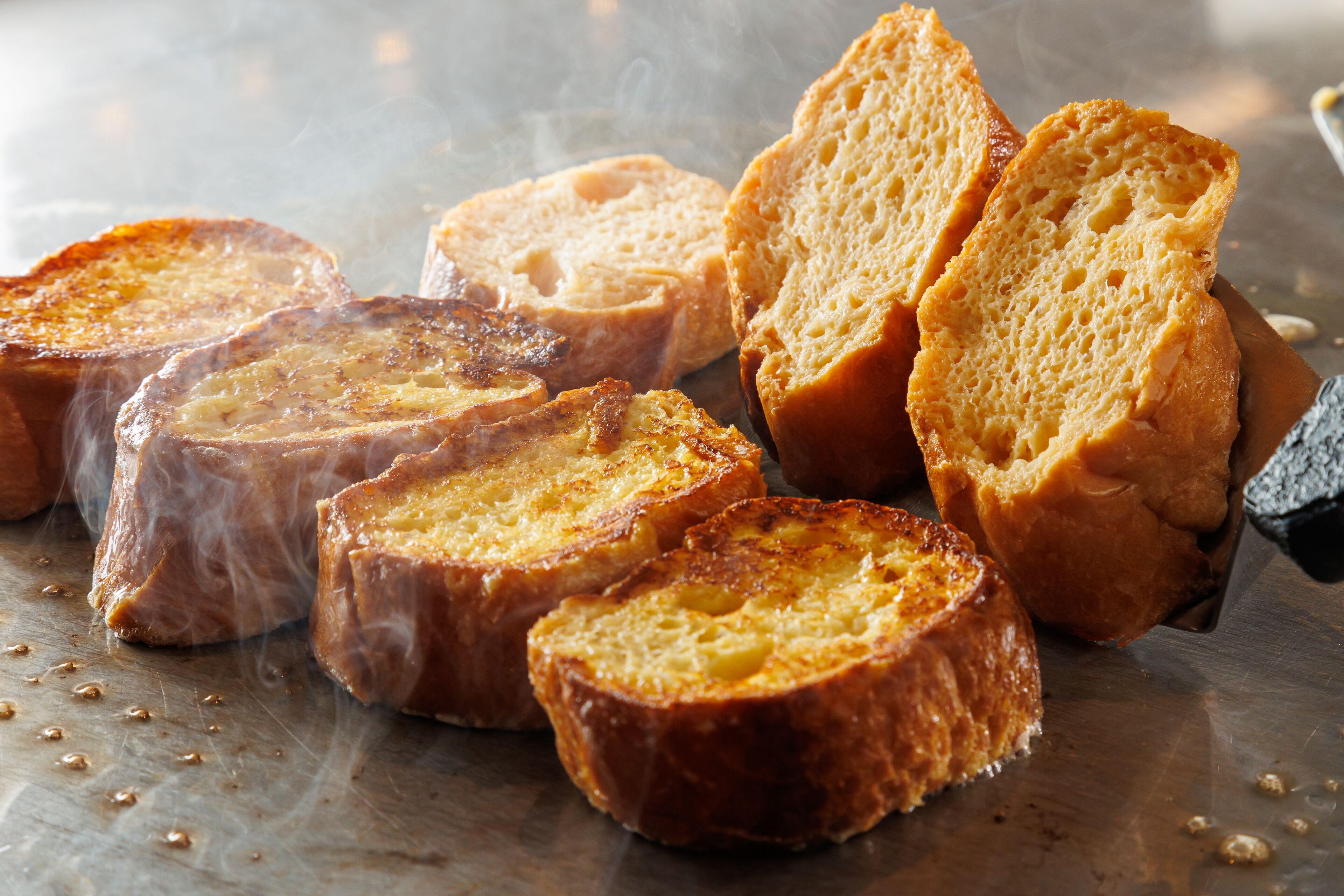Slices of toasted bread on a metal surface with steam rising from them.