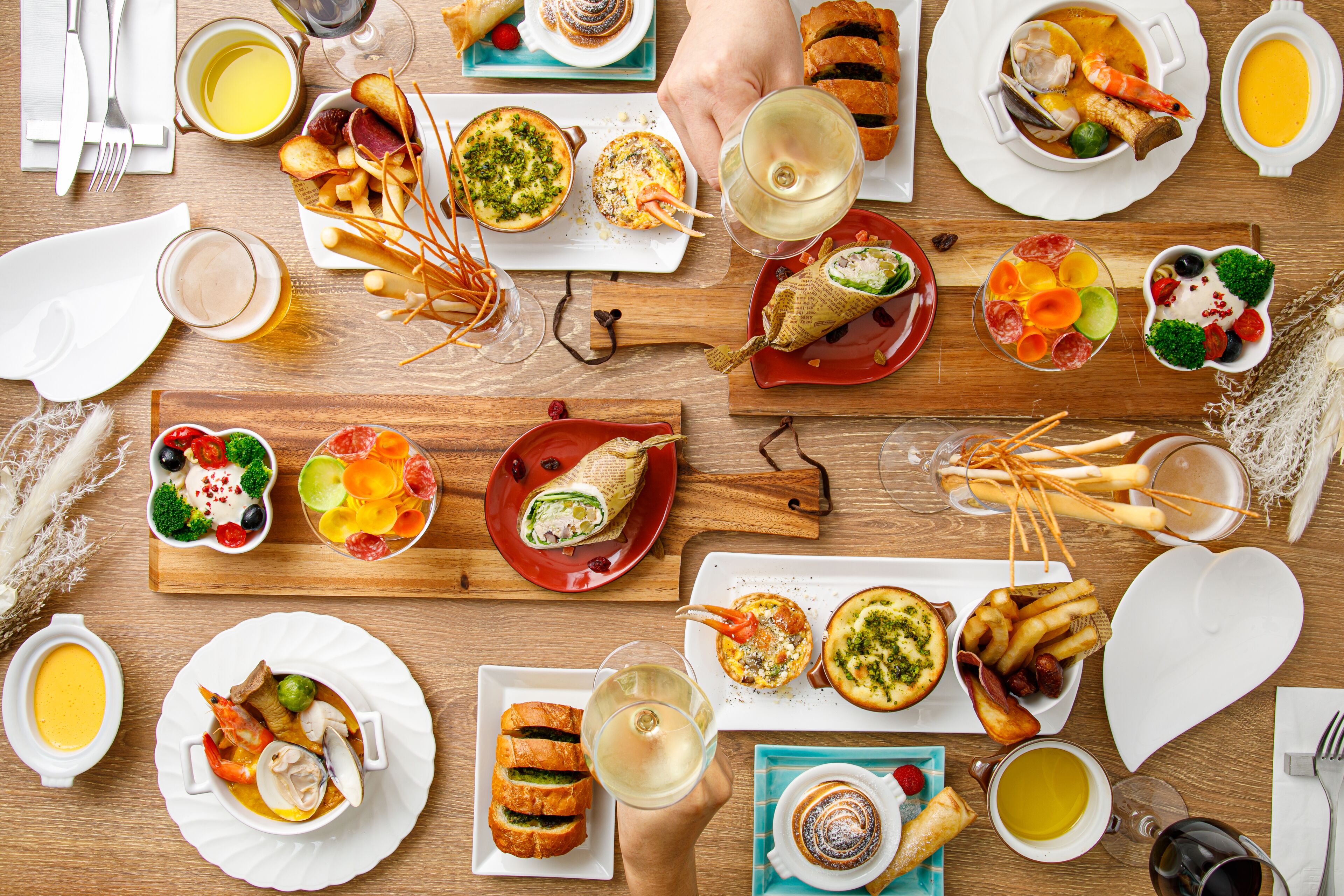 Una variedad de platos y bebidas sobre una mesa de madera, incluyendo mariscos, pan y una copa de vino.
