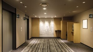 Een hotelgang met een kamerbreed tapijt, inbouwspots en een groot wandtapijt.