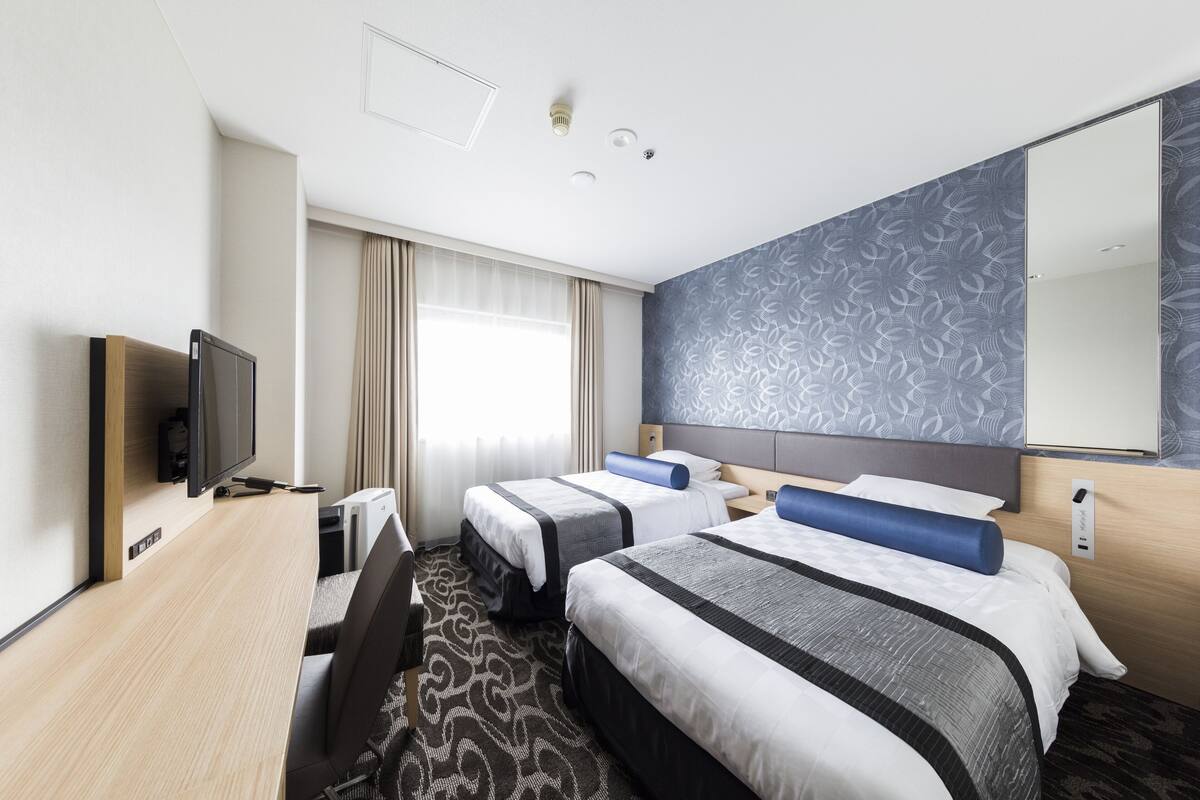 A hotel room with two beds, a desk with a computer, a TV, and a large mirror.
