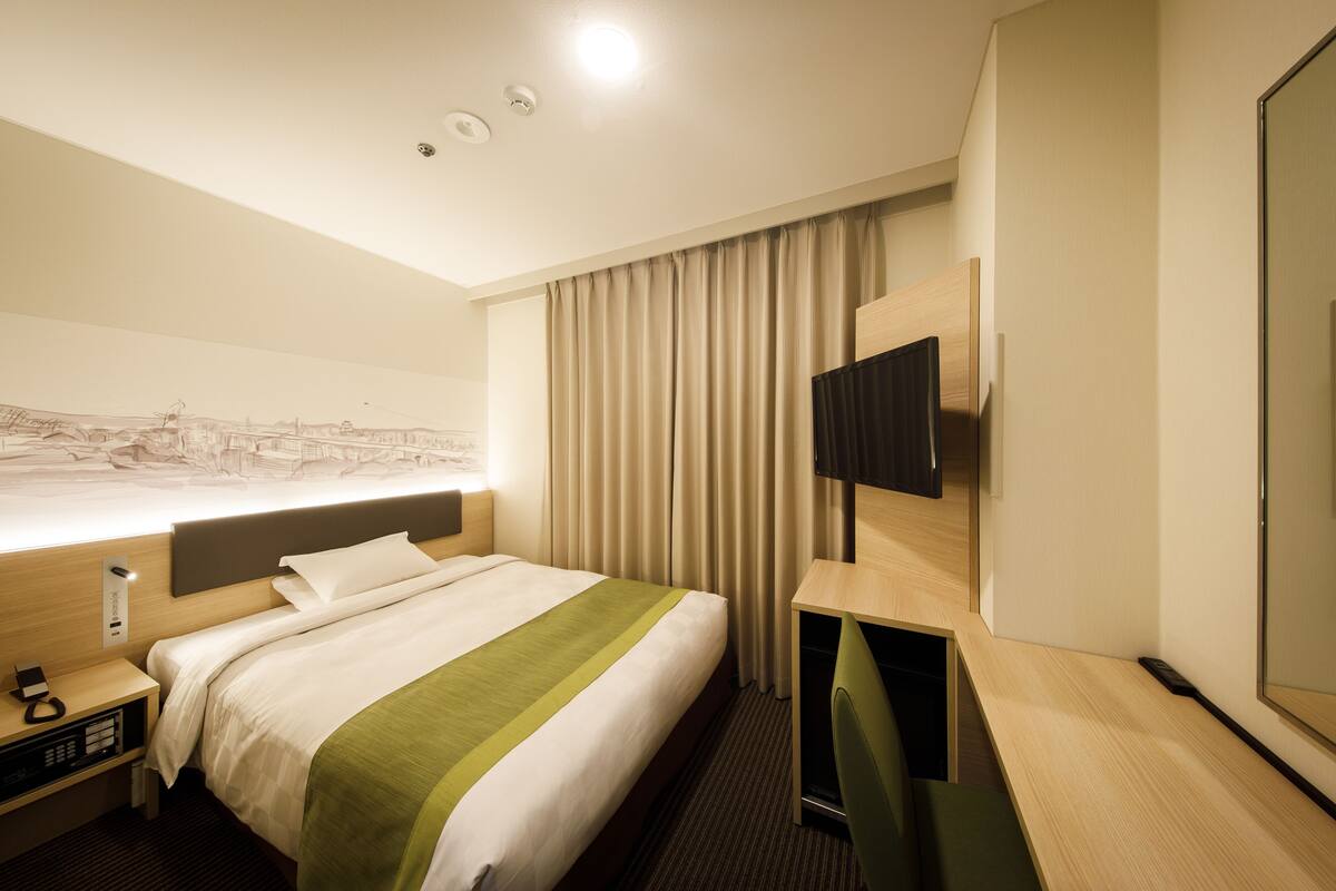 A hotel room with a bed, a desk, a chair, a TV, and a large window with curtains.
