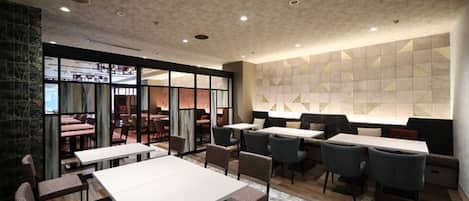Un restaurante moderno con diversas opciones de asientos, incluyendo mesas y cabinas, y un amplio ventanal que ofrece vistas al área de comedor.