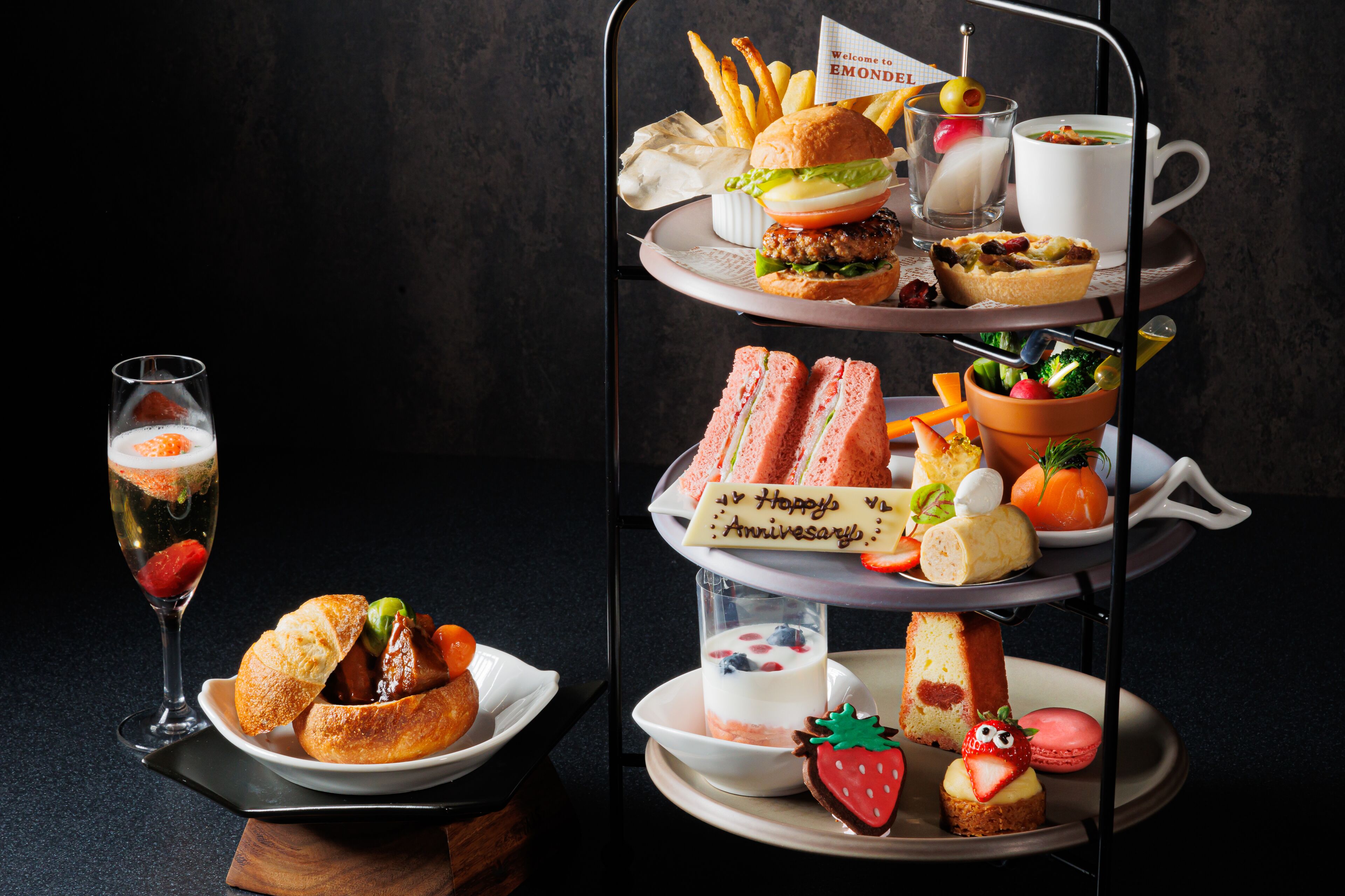 A tiered serving tray with various foods and a glass of champagne.