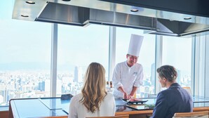 Un chef prepara comida en una cocina moderna con vistas a la ciudad.