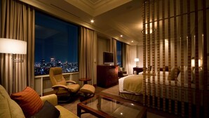Habitación de hotel con vista a la ciudad, una cama, un sofá, un televisor y un escritorio.