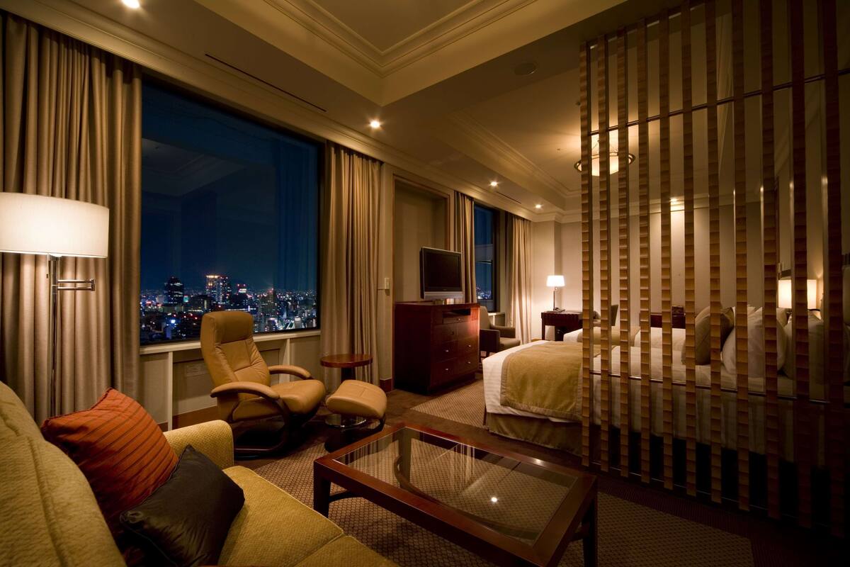 A hotel room with a city view, a bed, a sofa, a TV, and a desk.