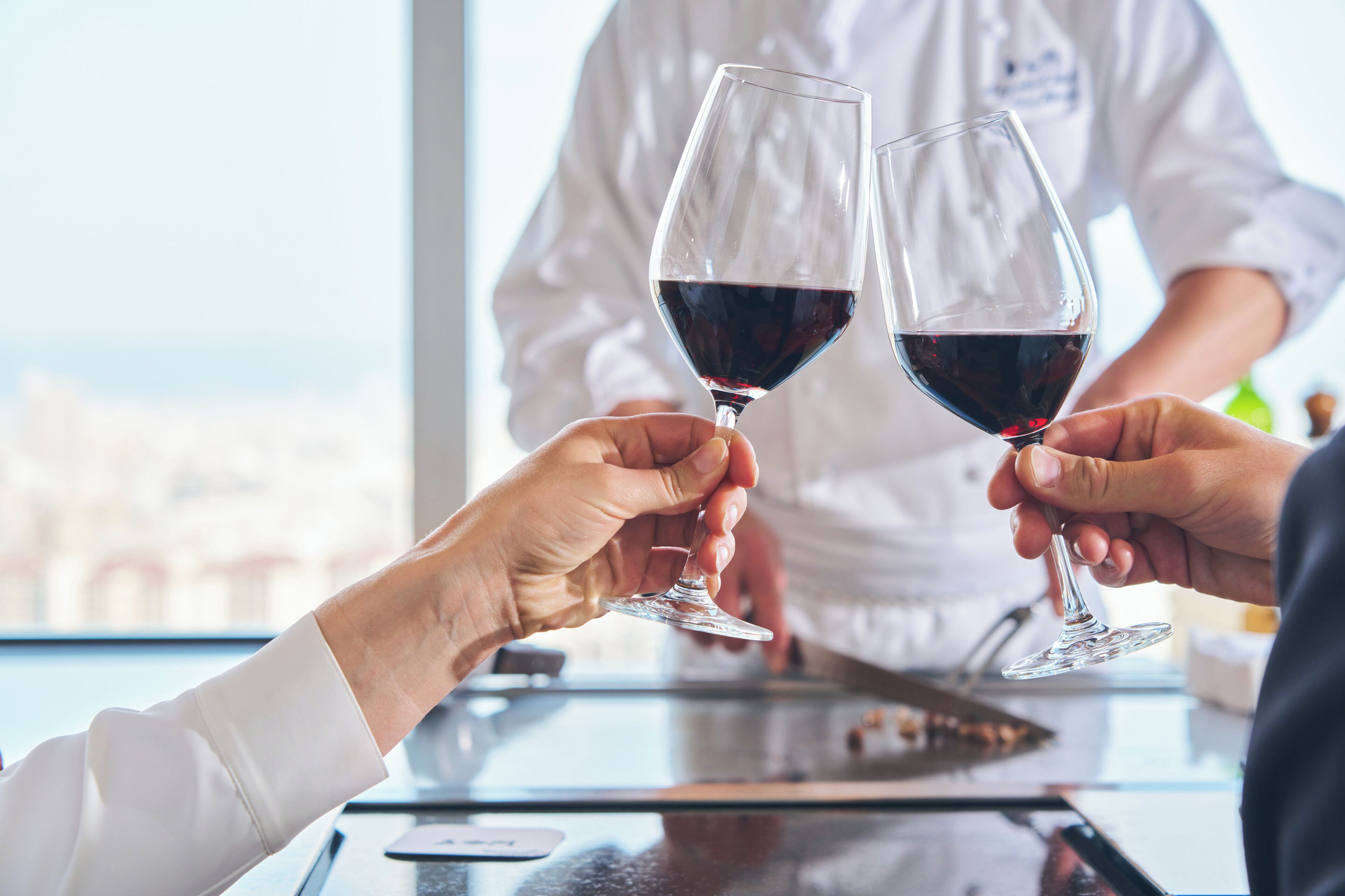 Two people holding wine glasses at a table with a view of buildings outside.