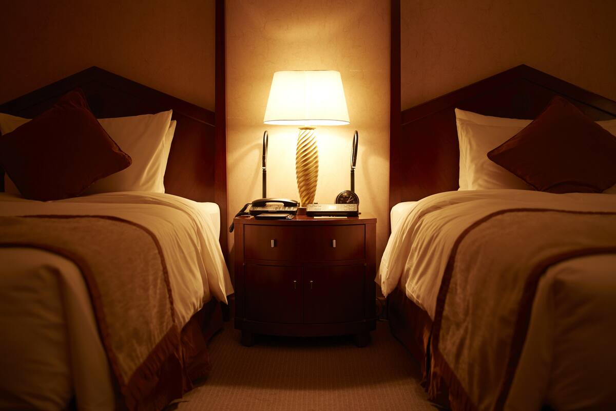 A hotel room with two beds, a nightstand with a lamp, and a small cabinet.