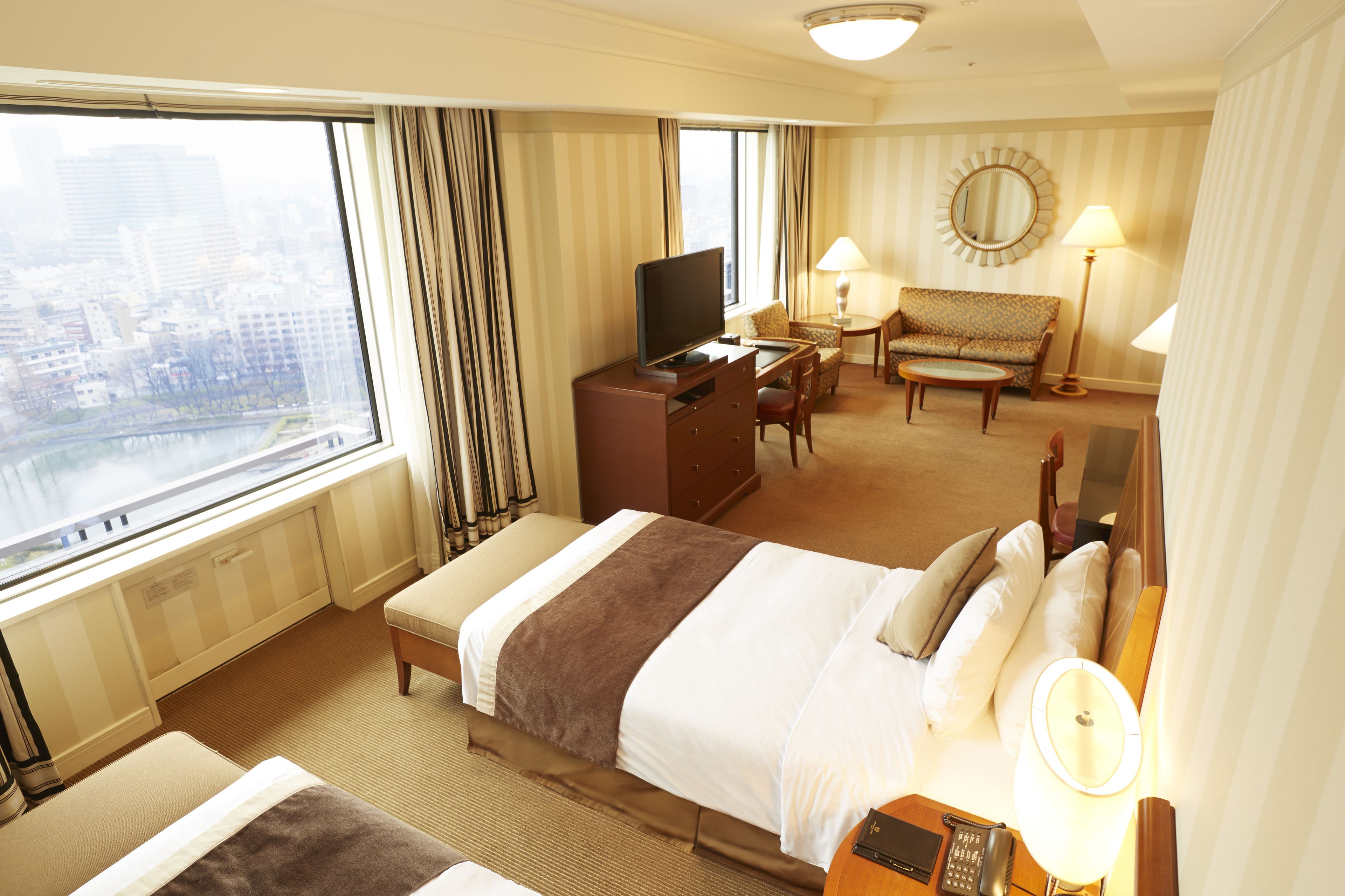 Una habitación de hotel con cama, escritorio, silla, televisión y vista a la ciudad.