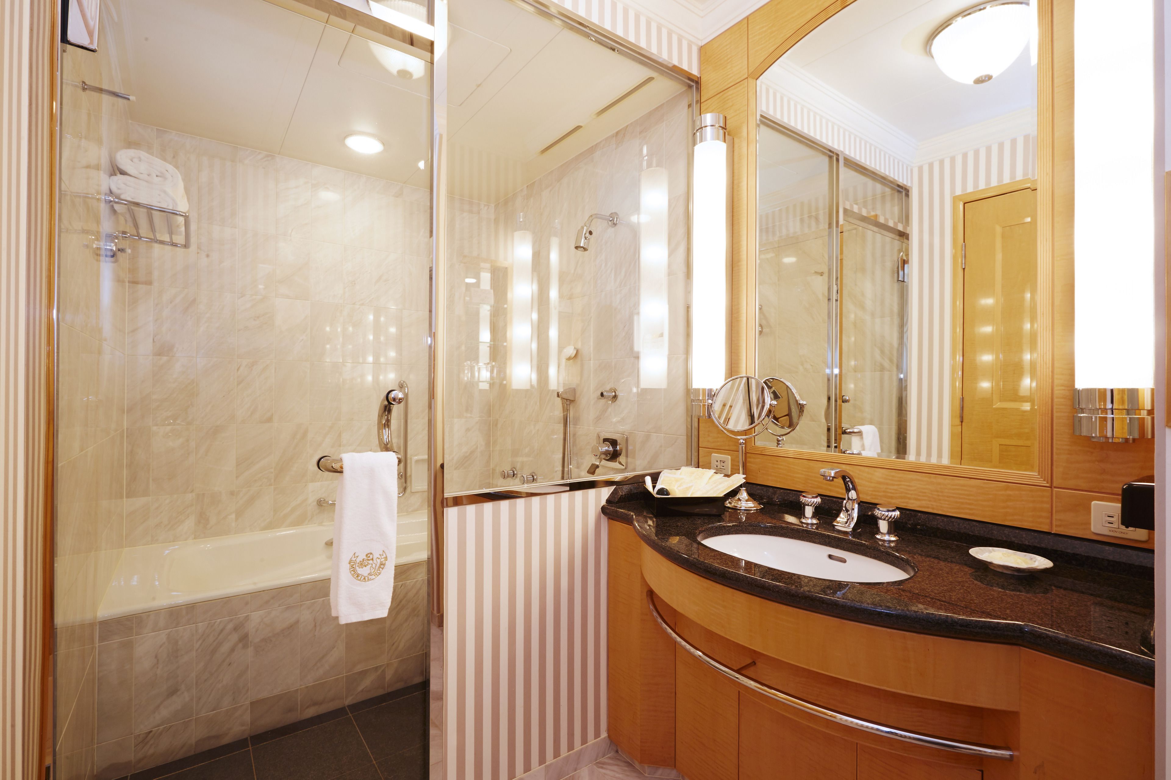 Un baño moderno con ducha envuelta en vidrio, una bañera independiente, un tocador con lavabo y un espejo grande.