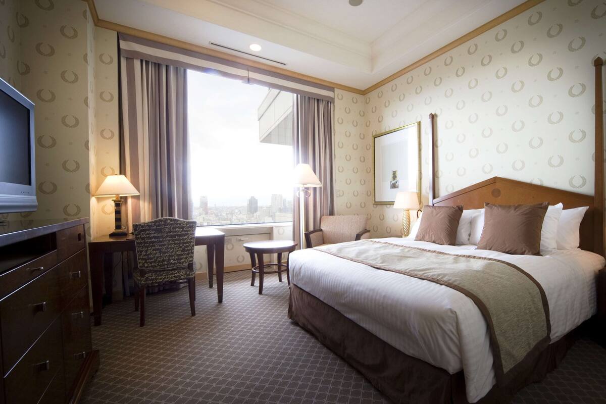 A hotel room with a large bed, a desk with a chair, a TV, and a window with curtains.
