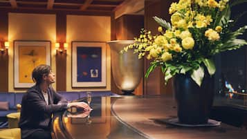 A man sitting at a bar with a large vase of yellow flowers, framed artwork on the wall, and a large metal bowl.