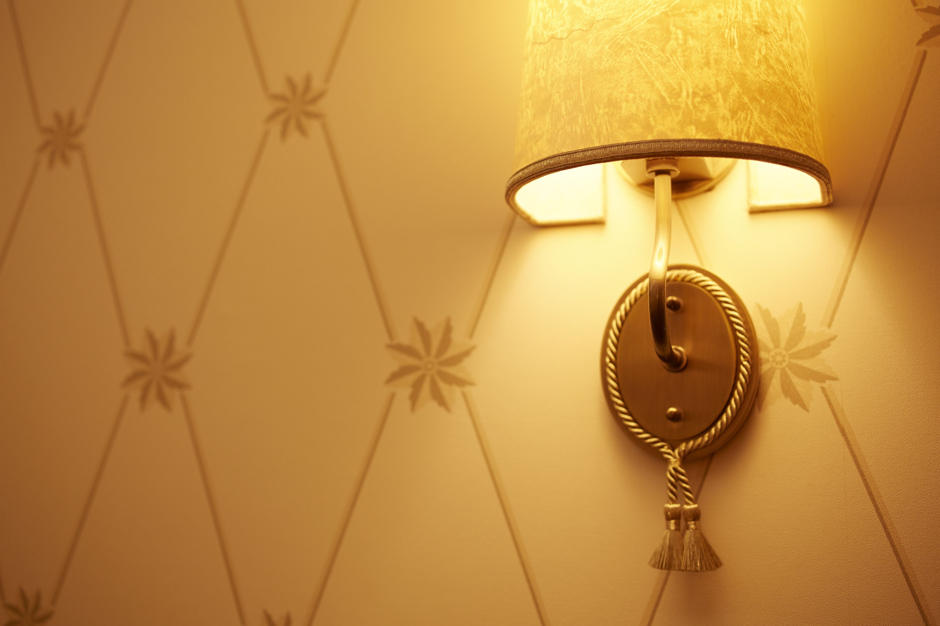 A wall-mounted lamp with a tassel, set against a wallpaper with a geometric pattern.