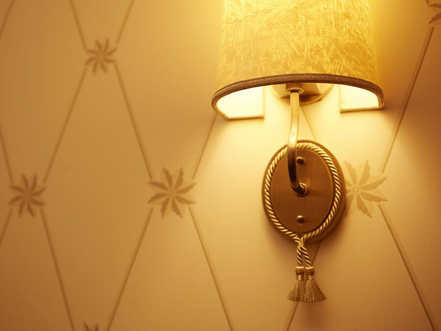 A wall-mounted lamp with a tassel, set against a wallpaper with a geometric pattern.
