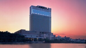 Un hotel moderno de gran altura con fachada de vidrio, situado cerca del agua y con un atardecer de fondo.