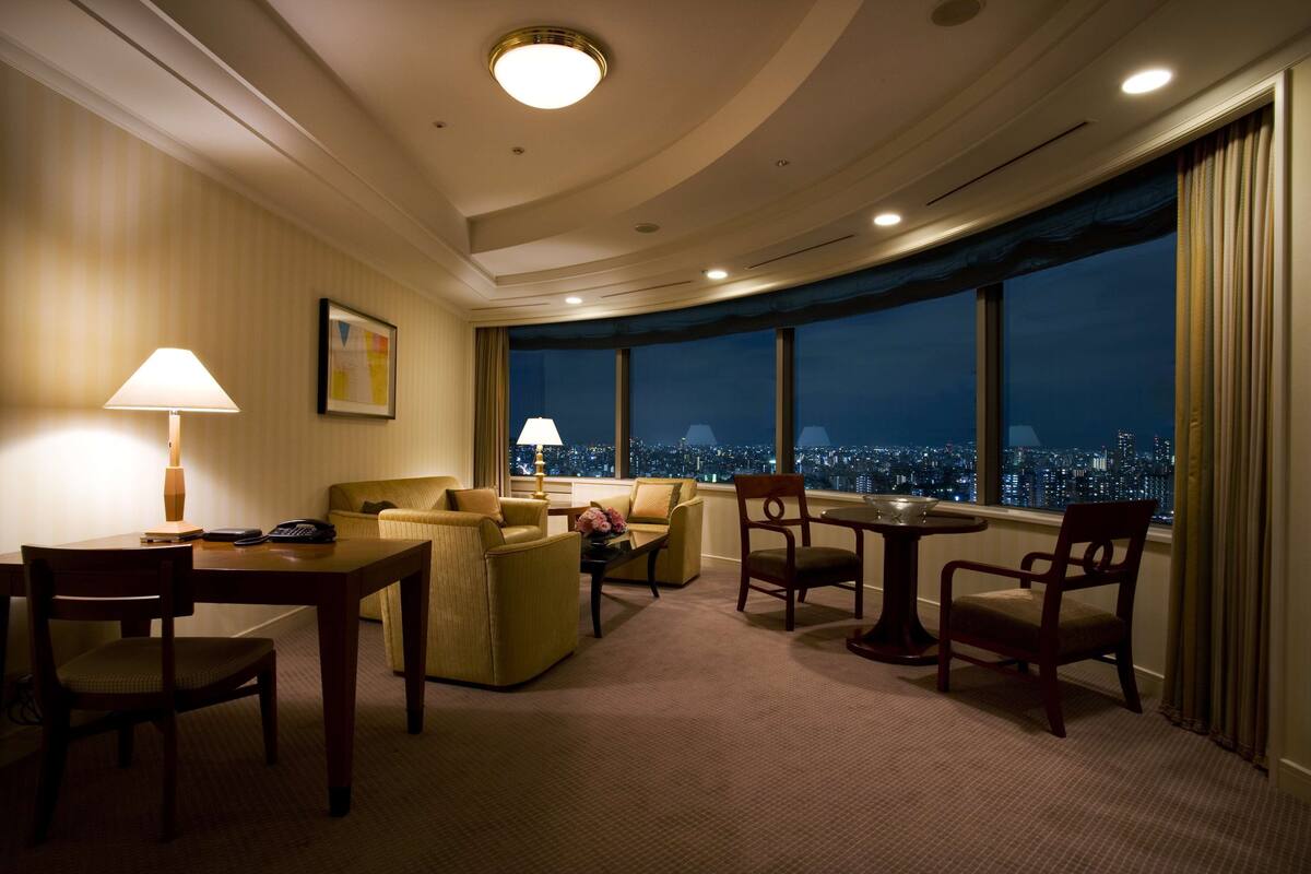 A hotel room with a city view, a dining area, and a seating area with a table and chairs.