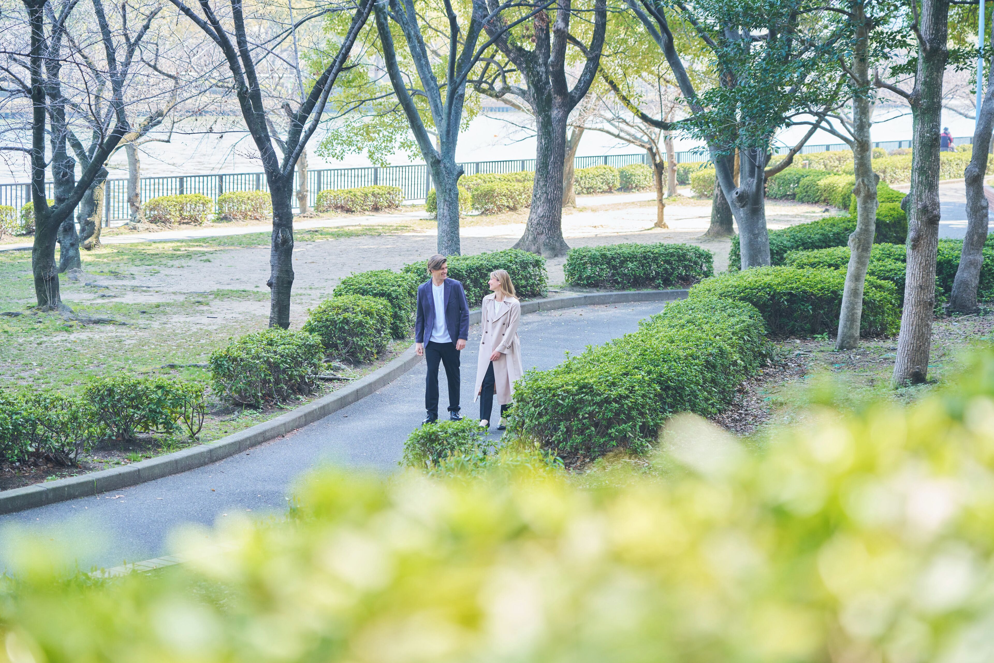 A couple walking on a curved pathway surrounded by trees and bushes.