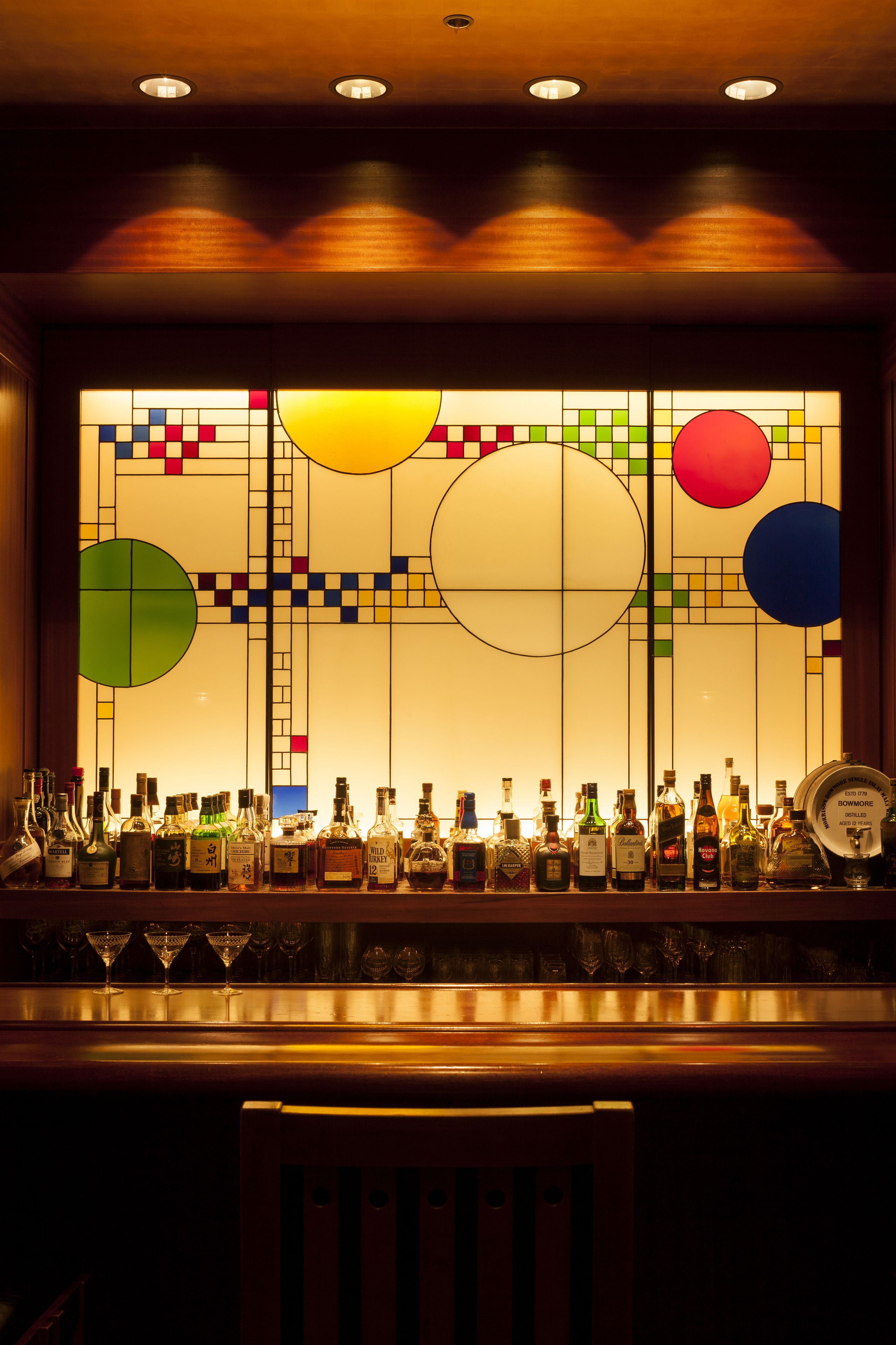 Un espace bar avec un assortiment de bouteilles d’alcool et de verres, éclairé par des luminaires au plafond.