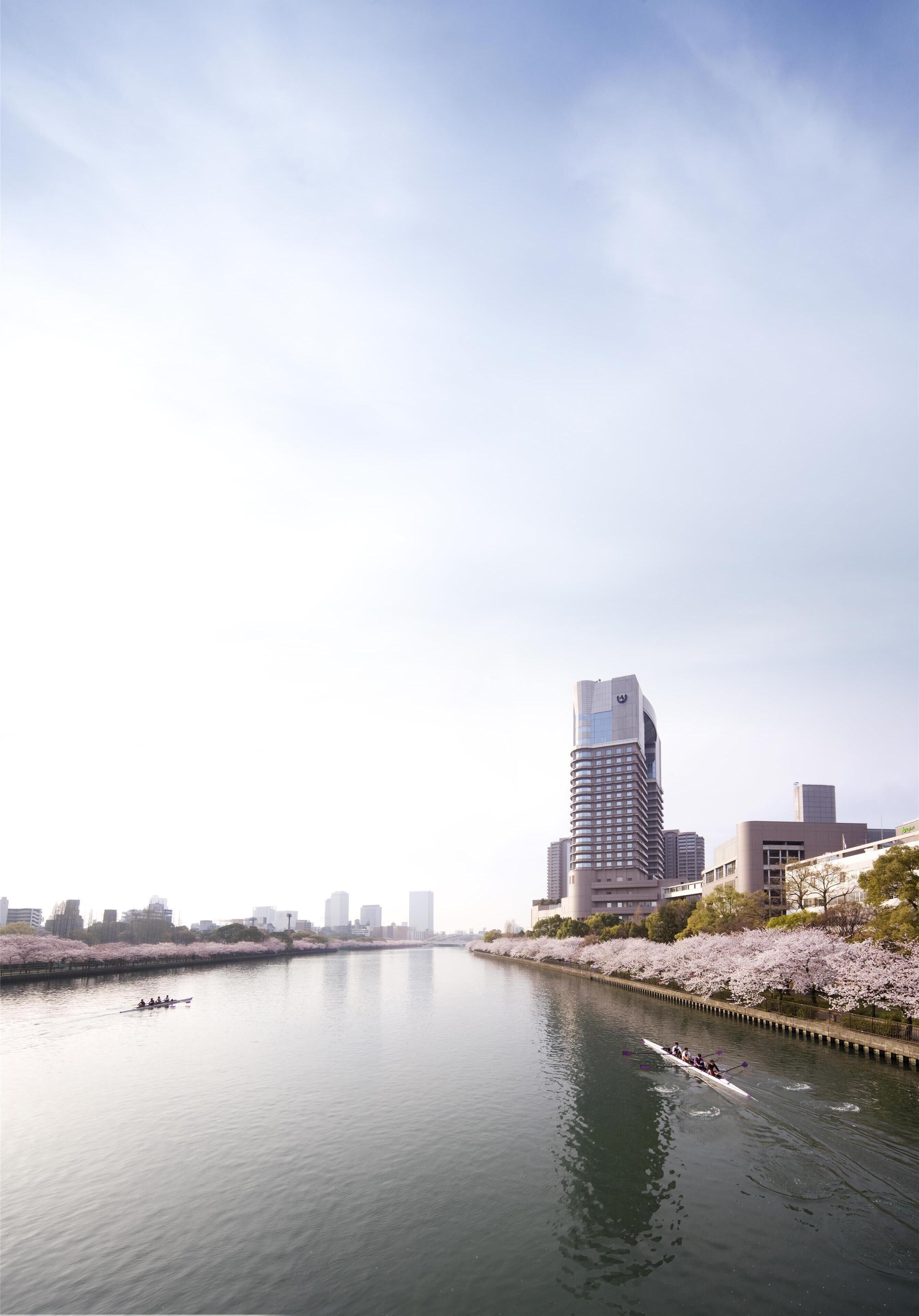 Un río con barcos, un edificio moderno y cerezos en flor a lo largo de las orillas.