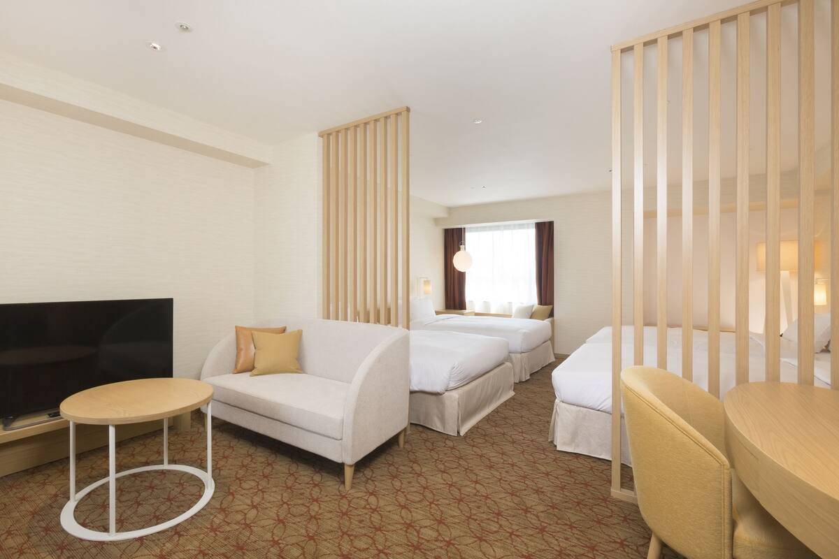 Ein Hotelzimmer mit Fernseher, zwei Betten, einer Schlafcouch und einem kleinen runden Tisch.