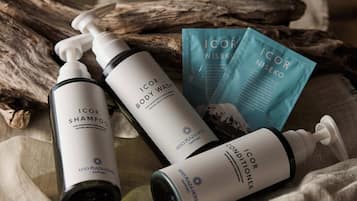 Three bottles of Icon body wash and conditioner, and two sachets of Icon body wash, placed on a fabric surface with a piece of driftwood in the background.