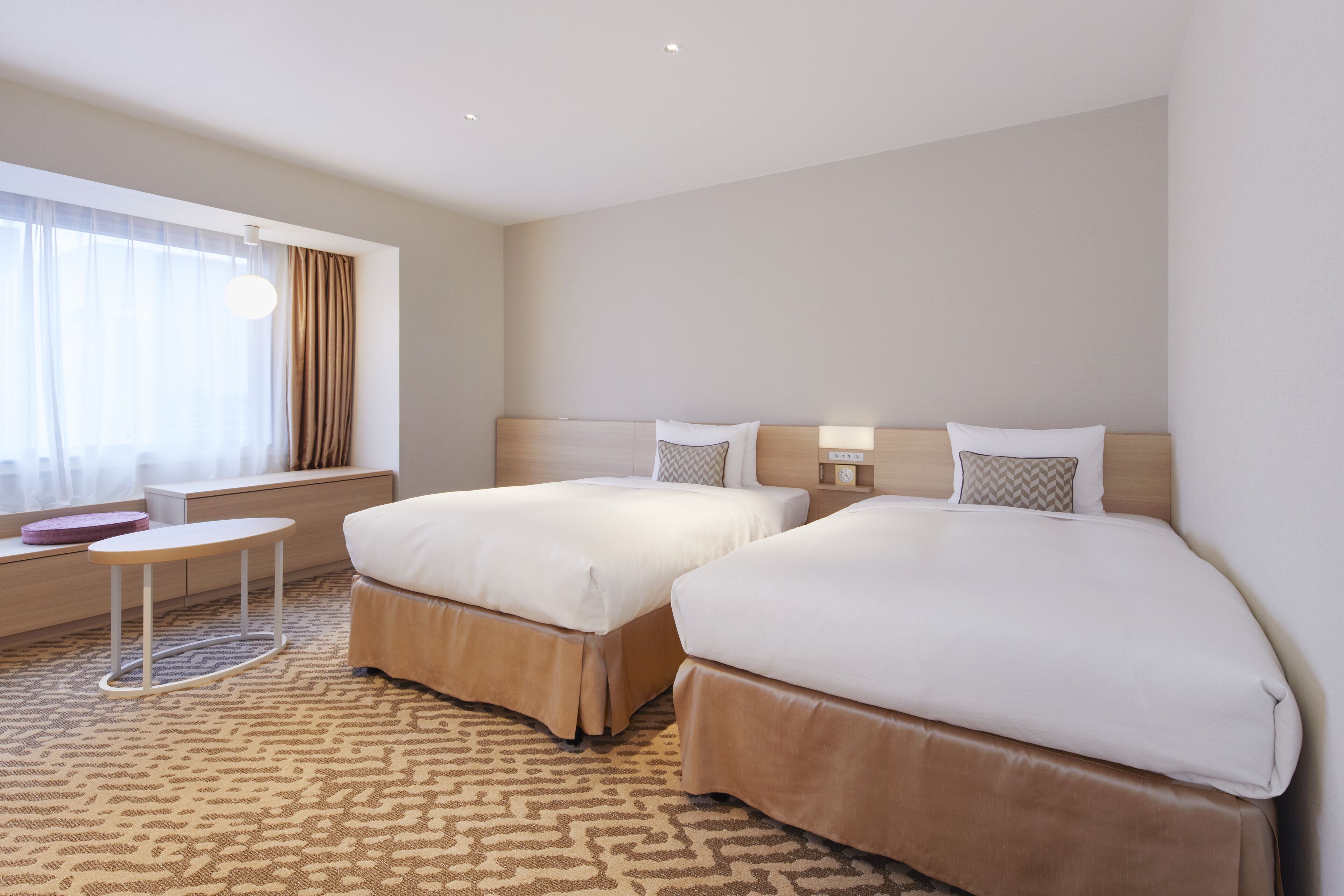Habitación de hotel con dos camas, una mesita y un ventanal con cortinas.