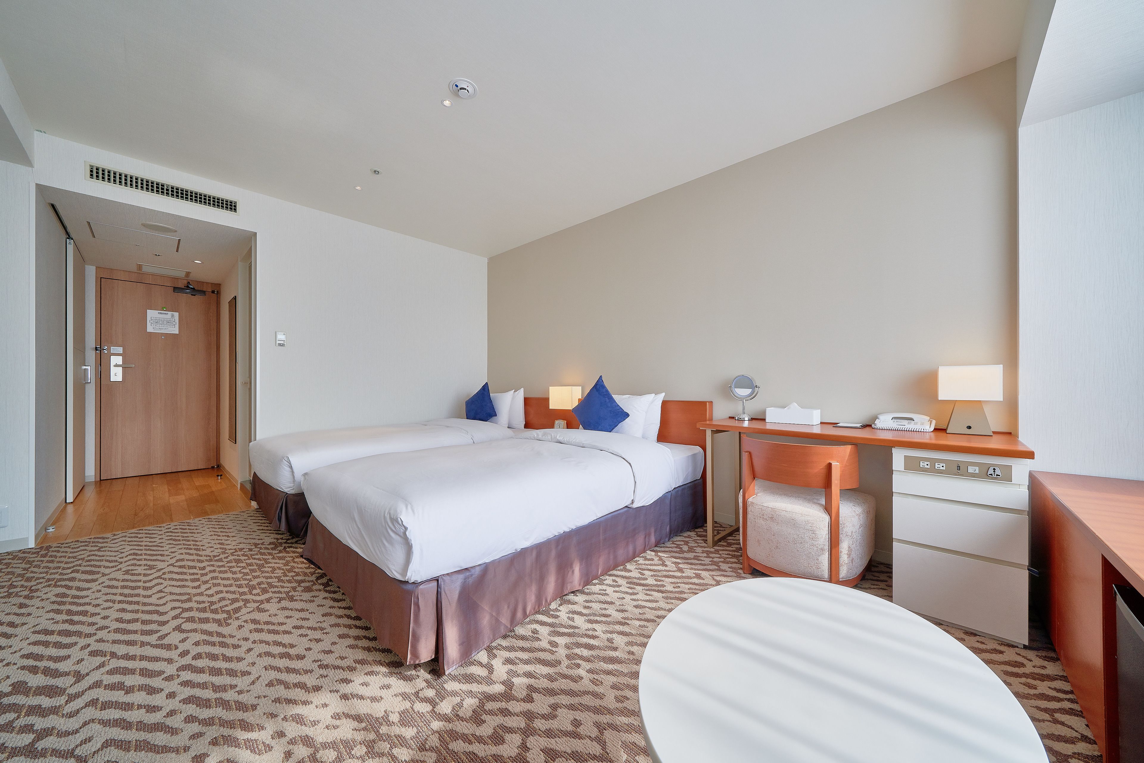 A hotel room with a large bed, a desk, a chair, and a small table.