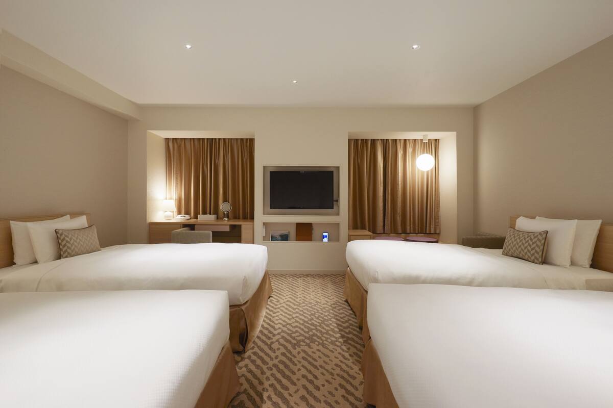 Ein Hotelzimmer mit zwei Betten, einem Fernseher, einem Schreibtisch und einem Spiegel.