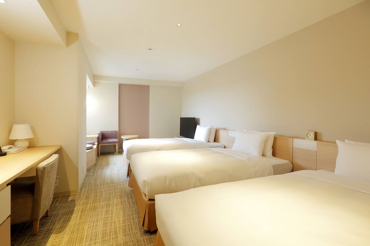 Ein Hotelzimmer mit drei Betten, einem Schreibtisch und einem Stuhl.