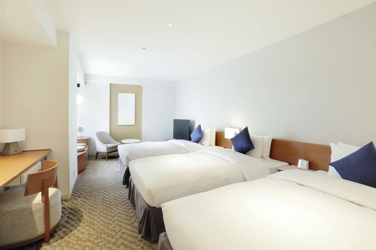 Ein Hotelzimmer mit drei Betten, einem Schreibtisch, einem Stuhl und einem kleinen Tisch.