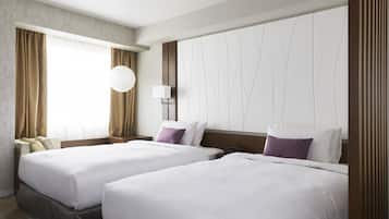 A hotel room with two beds, a large window with curtains, a wall-mounted lamp, and a round light fixture.