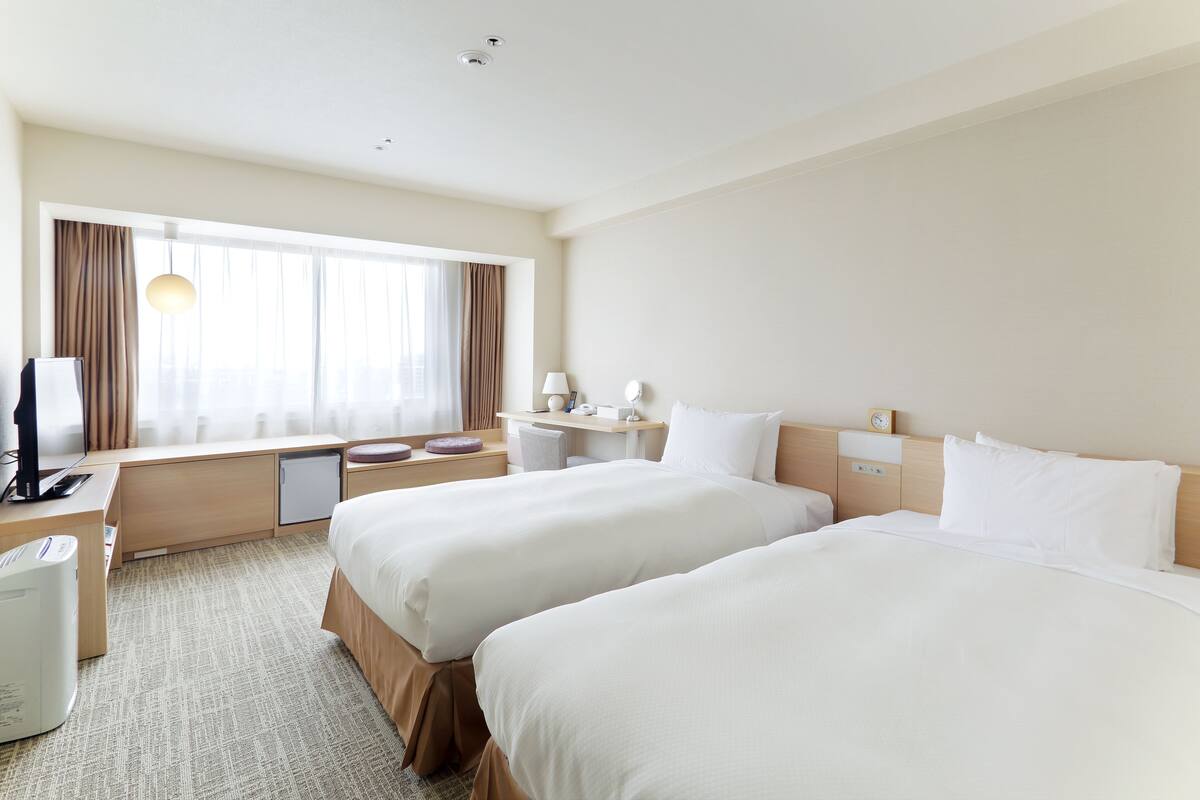 Ein Hotelzimmer mit zwei Betten, einem Schreibtisch, einem Stuhl, einer Lampe und einem kleinen Tisch.