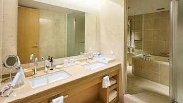 A modern bathroom with a large mirror, two sinks, a shower, and a vanity with a towel rack.