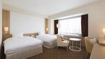 A hotel room with two beds, a small round table, two armchairs, a sofa, and a window with curtains.