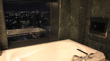 Un baño moderno con una bañera grande, una ventana con vistas a la ciudad y paredes de mármol.