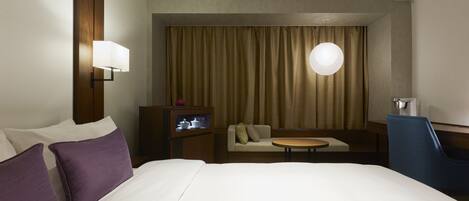 Quarto de hotel com uma cama grande, um sofá, uma mesa pequena e uma televisão.