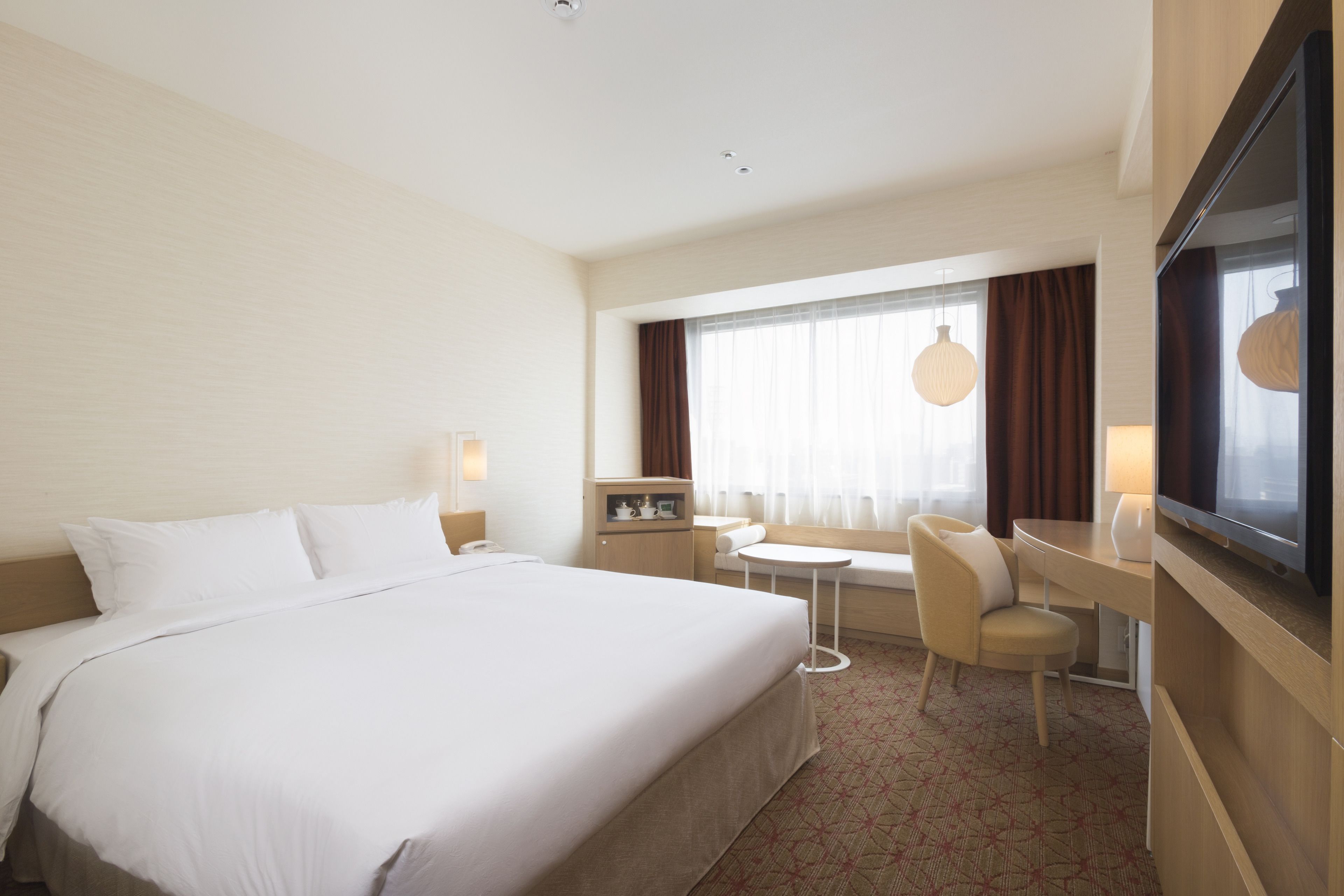 Una habitación de hotel con una cama grande, un escritorio, una silla, un televisor y una ventana con cortinas.