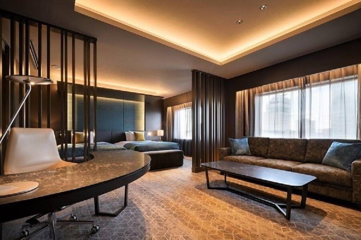 A modern hotel room with a round table, a sofa, and a bed with a headboard.